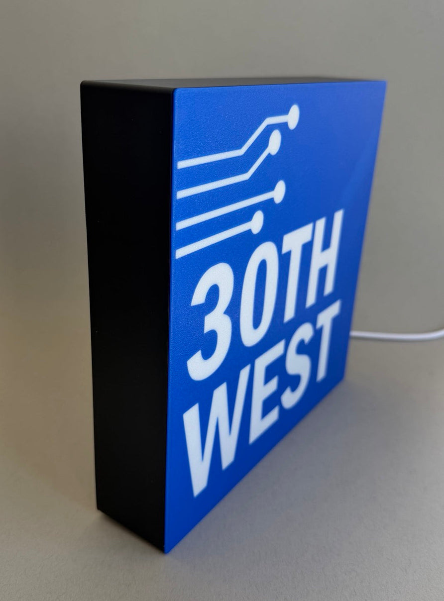 Blue and black sign with '30th West' on a gray surface